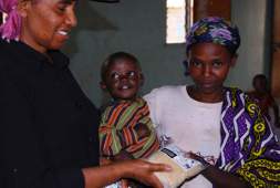 Our founder AlyceJo gives a bag of rice to a mother and her grinning toddler